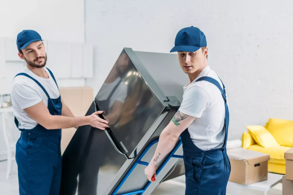 Doha Movers Packers two movers in uniform using hand truck while transporting refrigerator in apartment
